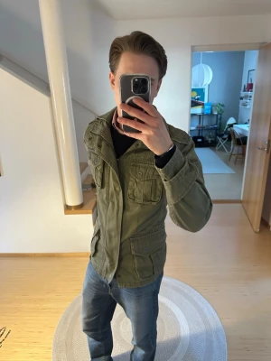 Olivgrön parkajacka från Alpha Industries - Säljer en olivgrön vintage field jacket från Jack & Jones med flera fickor och dragkedja framtill. Jackan har en militärinspirerad look och är tillverkad i slitstark bomull. Härlig vår jacka perfekt till både vår, sommar och höst