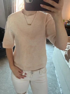 Ljusbeige stickad tröja med kort ärm - Söt ljusbeige stickad tröja med korta ärmar och rund halsringning. Tröjan har en enkel, stilren design och ribbade muddar vid ärmslut och nederkant. Perfekt för en avslappnad och trendig look. Väldigt skön mot kroppen och inte alls stickig.