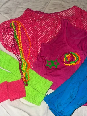 80-tals neon maskeradset - Färgglatt 80-tals maskeradset med rosa nättröja, rosa linne, blåa tights, gröna  benvärmare, rosa handledsvärmare,  neonfärgade pärlhalsband och örhängen i form av stjärnor. Perfekt för temafest eller cosplay med retrovibbar. Endast använd 1 gång och inga tecken på användning!! OBS: shortsen följer inte med. 🫶 STRETCHIGA MATERIAL SÅ PASSAR ALLA FRÅN XS-M (kanske L)