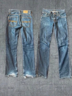 Flared  Nudie Jeans - Snygga blå slim fit jeans från Nudie Jeans med slitna detaljer och råa kanter vid bensluten. Klassisk femficksmodell med orange sömmar och Nudie-logga på bakfickan. Tillverkade i 100% bomull för en autentisk jeanskänsla.