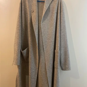 Grå Amisu hoodie/cardigan - Lång, gråmelerad hoodie/cardigan i mjukt material med stora fickor och dragkedjor vid ärmslut och sidor. Köpt från New Yorker. Perfekt för en chill och avslappnad look!