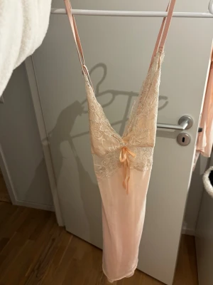 Ljusrosa spetsnattlinne med rosett - Sött/sexigt ljusrosa nattlinne med tunna axelband och v-ringning. Överdelen är dekorerad med vacker spets och en liten rosett framtill. 