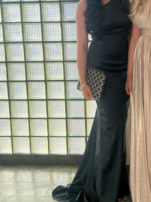 Svart oneshoulder långklänning - Säljer en elegant svart långklänning med oneshoulder-design. Klänningen har en figurnära passform och är tillverkad i ett slätt material som ger en stilren look. Perfekt för bal eller festliga tillfällen.