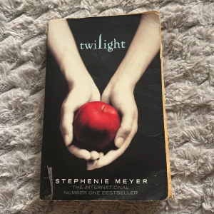 Twilight av Stephenie Meyer - Twilight av Stephenie Meyer är en internationell bästsäljare inom ungdomslitteratur. Omslaget är svart med motiv av två händer som håller ett rött äpple. Boken är på engelska och har mjuka pärmar. Perfekt för dig som gillar romantik och fantasy med vampyrtema.