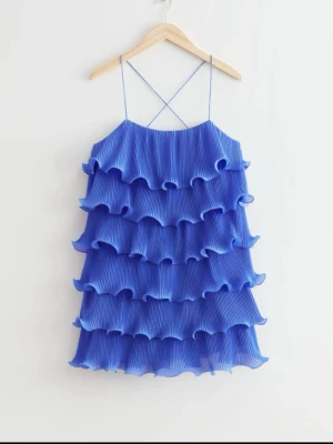 Blå volangklänning med tunna band - Supersöt blå volang klänning med tunna axelband som korsas i ryggen. Perfekt till sommaren!