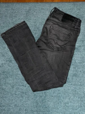 Grå Jack & Jones glenn - Storlek W30 L32. Modell: Glenn original. Säljer ett par grå slim fit jeans med klassisk femficksdesign och svarta sömmar. Jeansen har en diskret tvättad look och sitter tajt längs benen för en modern stil. Perfekta till sneakers och t-shirt för en avslappnad vibe.
