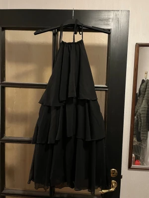 Svart volangklänning med öppen rygg - Snygg svart kortklänning med volanger och halterneck. Klänningen har öppen rygg och knyt i nacken, vilket ger en cool och luftig känsla. Aldrig använd. Skriv för fler bilder eller frågor🩷