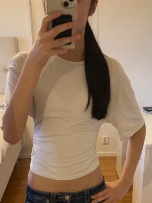 Vit croppad topp med snörning - Snygg vit croppad topp med korta ärmar och rund halsringning. Toppen har en cool snörningsdetalj i sidan som ger en trendig look. Perfekt att matcha med höga jeans eller kjol för en avslappnad stil.