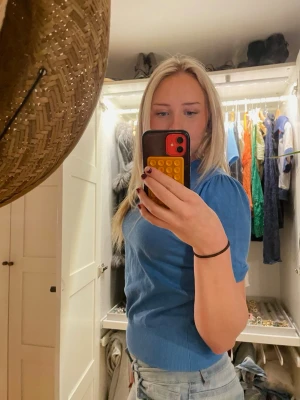 Blå topp med puffärm - Säljer en blå topp med korta ärmar och rund hals. Toppen har en vanlig passform för storlek S och är tillverkad i mjukt material som sitter bekvämt mot kroppen. Perfekt att styla med jeans eller kjol. 