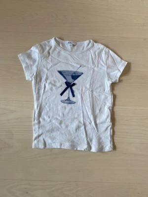 Vit t-shirt med martiniglas från Subdued - Supersöt vit croppad t-shirt från Subdued med ett tryck av ett blått martiniglas. Är i storlek M men passar även S. 🤍köpt på Subdued utomlands.