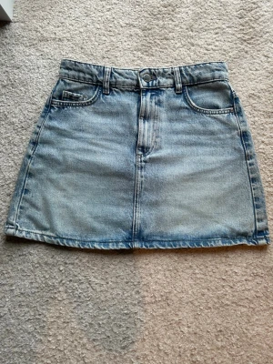 Blå jeanskjol från Zara - Säljer en klassisk blå jeanskjol från Zara i xs. Kjolen har en ganska kort och en medelhög midja. Endast använd ett fåtal gånger. Perfekt till sommaren!!