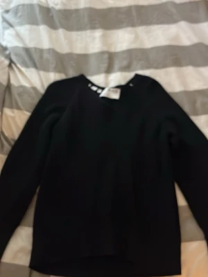 Svart stickad tröja från Filippa K - Klassisk svart stickad tröja från Filippa K med rund halsringning och långa ärmar. Tröjan har ribbstickade muddar vid ärmslut och nederkant, vilket ger en snygg och enkel look. Perfekt basplagg till garderoben.