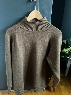 Brun stickad tröja från Jack & Jones - Snygg brun stickad tröja från Jack & Jones med hög, ribbad polokrage och långa ärmar. Tröjan har en enkel, stilren design och är perfekt för kyligare dagar. Materialet känns mjukt och bekvämt mot huden. 