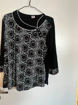 Svart och vit blus med blommönster - Unik blus från Mia Moda i svart och vitt med blommigt mönster och röda detaljer. Trekvartsärm med mönstrade muddar och lös passform. Perfekt för dig som gillar att sticka ut med coola mönster och kontraster. Rök och djurfritt hem. Pruta gärna !🌸