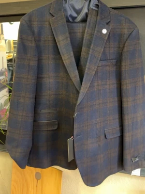 Rutig blåbrun kostymkavaj & väst & byxor - Snygg tvådelad kostym med kavaj och matchande väst och byxor i mörkblått och brunt rutigt mönster. Klassisk passform med smala slag, flera fickor och knappar framtill. Perfekt för dig som vill ha en stilren och modern look.