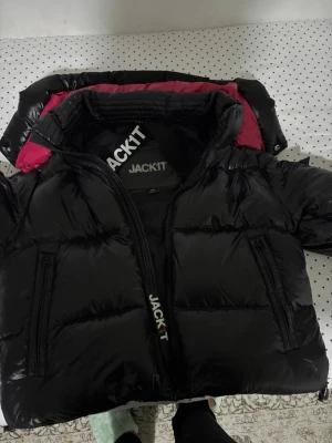 Svart pufferjacka från JACKIT - Snygg svart pufferjacka från JACKIT med glansig finish och kontrasterande mörkrosa innerfoder. Jag köpte jackan för 2500 nypris och säljer den för detta priset. Vid snabbköp var gärna säkra och prisförslag är alltid välkomna 