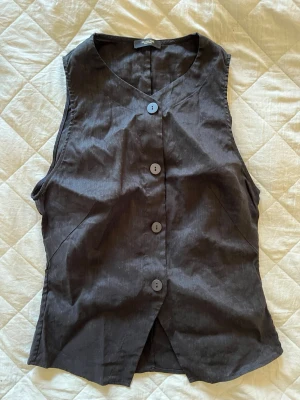 Svart väst från Massimo dutti - Stilren svart väst i linne/viskos från Massimo dutti i storlek S. Har  fyra stora knappar framtill, Västen har en klassisk, rak passform och är ärmlös med v-ringad hals. Är aldrig använd