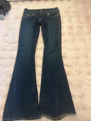 Blå bootcut jeans från True Religion - Säljer ett par mörkblå bootcut jeans från True Religion med ikoniska fickdetaljer och kontrastsömmar 🥂