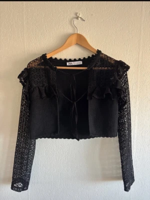 Stickad spets kofta - Super söt kort, svart stickad spetskofta med volanger, som går att knyta. Endast använd ett fåtal gånger! 