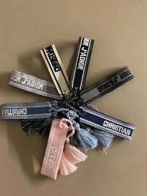 Christian Dior broderade armband - LÄS!!! Säljer ENDAST d mörkblåa och d begiea. broderade armband från Christian Dior i beige och mörkblått. Armbanden har tofsar i ändarna och texten 'Christian Dior' eller 'J'ADIOR' broderat på bandet. Perfekt accessoar för att lyfta din outfit.