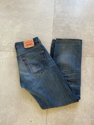 Levi's 501 blå jeans, storlek W29 L32, Vintage  - Klassiska blå Levi's 501 jeans i rak modell med fem fickor och ikonisk läderpatch bak i midjan. Jeansen har en snygg tvättad look och är tillverkade i slitstark denim. Perfekta för en avslappnad och tidlös stil.