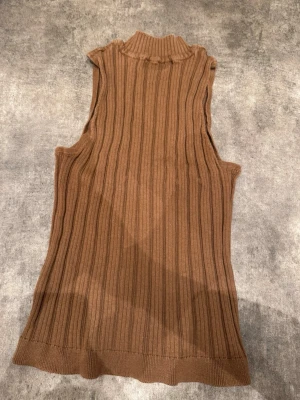 Brun ribbad polotopp från Object - Snygg brun ribbad polotopp från Object. Ärmlös modell med hög krage och mjukt, stretchigt material som sitter skönt. Perfekt att styla med jeans eller kjol för en trendig look.