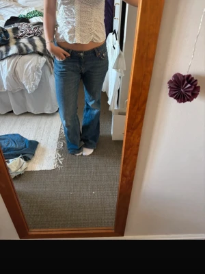 Blå flared jeans med låg midja - Säljer ett par klassiska blå jeans med låg midja och flared ben. Jeansen har fem fickor och en enkel, tidlös tvätt. Perfekta för en avslappnad och trendig look. Materialet är denim i bomull och passformen är lite lösare över benen.