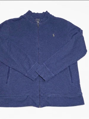 Blå ziptröja från Polo Ralph Lauren - Mörkblå ziptröja från Polo Ralph Lauren med liten broderad logga på bröstet. Tröjan har hög krage, dragkedja framtill och två fickor. Tillverkad i mjukt bomullsmaterial och har långa ärmar med ribbade muddar.