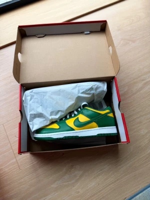 Nike Dunk Low ”brazil” sneaker - Nike Dunk Low sneakers i grön och gul färg med vita skosnören och sula. Klassisk låg siluett med perforerad tåbox och ikonisk Swoosh-logga på sidan. Ovandelen är i läder och skon har en retro vibe som sticker ut.