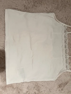 Vit linnetopp med spetskant - Söt vit linnetopp med tunna axelband och dekorativ spetskant upptill. Perfekt för varma dagar eller som layering-plagg. Enkel och stilren design som passar till det mesta.