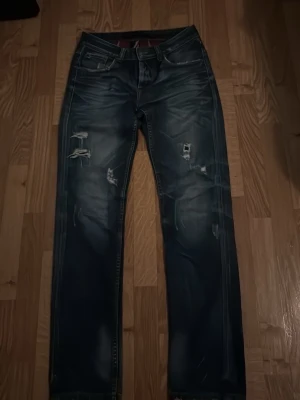 Mörkblå slitna jeans med raka ben - Säljer ett par mörkblå jeans med raka ben och slitna detaljer på framsidan. Jeansen har klassisk femficksdesign och markerade sömmar. Perfekta för en avslappnad och trendig look pris går även att diskuteras vid snabbaffär 