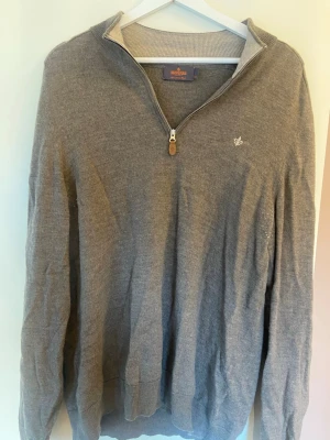 Grå halvzip-tröja från Morris - Snygg grå tröja från Morris med halv dragkedja och diskret broderad logga på bröstet. Tröjan har ribbade muddar och krage, perfekt för lager på lager. Tillverkad i mjukt material som känns skönt mot huden.