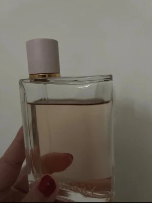 Burberry Her parfym rosa glasflaska - Säljer en Burberry Her parfym i en stilren, rektangulär glasflaska med ljusrosa lock och gulddetalj. Doften har en ljusrosa vätska som syns genom det klara glaset. Perfekt för dig som gillar eleganta och moderna parfymer.