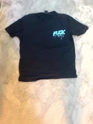 Svart t-shirt med blå graffiti-tryck - Cool svart t-shirt med stort blått graffiti-inspirerat tryck på ryggen och mindre tryck på bröstet. T-shirten har klassisk passform och korta ärmar. Perfekt för dig som gillar streetwear och statement-plagg.
