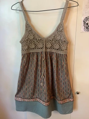 Beige vintage linnetopp med mönster - Supersöt vintage linnetopp med virkad överdel i beige och knyt framtill. Nedre delen har ett bohemiskt mönster i dova färger och en bred kant längst ner. Står ingen storlek men skulle uppskatta som en S/M eller 38.