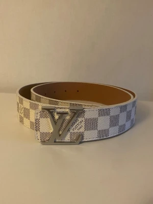 Vit Rutig bälte  - Snyggt bälte med klassiskt rutigt mönster i vitt och grått. Perfekt accessoar för att lyfta din outfit med en exklusiv touch.