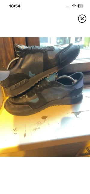 Valentino Garavani camo sneakers - Snygga sneakers från Valentino Garavani i svart och blått med camomönster. Skorna har svarta snören, detaljer i mocka och läder samt en cool gummisula med nitar på hälen. Perfekta för dig som vill sticka ut med exklusiv streetstyle.