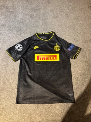 Inter Milan svart matchtröja Nike - Snygg svart Inter Milan matchtröja från Nike med gula detaljer och Pirelli-logga på bröstet. Champions League-märke på ärmen och namn samt nummer 'Lautaro 10' på ryggen. Tillverkad i lätt och ventilerande material, perfekt för fotboll eller träning.