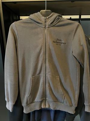 Grå zip hoodie från Peak Performance -  Säljer en grå zip hoodie från Peak Performance i bra skick, dragkedjan är lite trög men funkar fortfarande. Det är storlek 160 alltså junior storlek. Vid fler bilder/frågor är det bara att höra av sig, öppen för prisförslag.