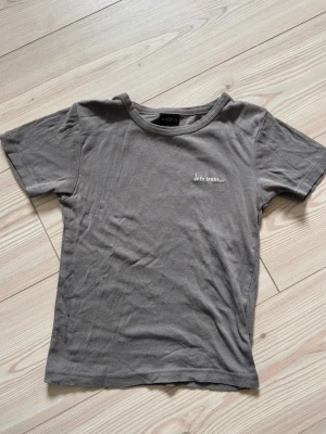 Grå t-shirt med broderad text - Säljer en enkel grå t-shirt från Monki med broderad text 'lets frans...' på bröstet. T-shirten har rund halsringning och korta ärmar.