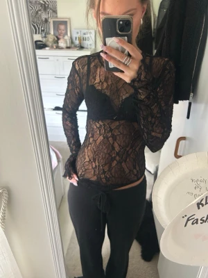 Svart spetsbody - Säljer en svart, transparent spetsbody med lång ärm och figurnära passform. Bodyn har vackra spetsdetaljer och är perfekt för dig som gillar en edgy och trendig stil. Superfin att styla med både jeans och kjol.