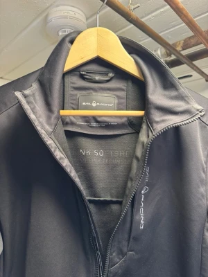 Svart vindjacka från Sail Racing - Snygg svart vindjacka från Sail Racing med hög krage och hel dragkedja framtill. Jackan har diskret logga på bröstet och är tillverkad i ett slätt, vindtätt material. Perfekt för dig som vill ha en stilren och funktionell jacka. Använd 4-5 gånger säljer för den är för liten för mig den passar S men bäst på xs