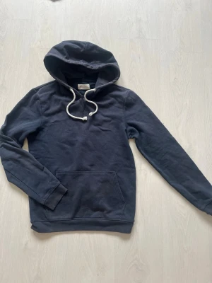 Mörkblå hoodie med huva och ficka - Snygg mörkblå hoodie från Pierone med klassisk känguruficka framtill och vit dragsko i huvan. Tillverkad i mjukt bomullsmaterial och har ribbade muddar vid ärmslut och nederkant. Perfekt för en avslappnad och stilren look.