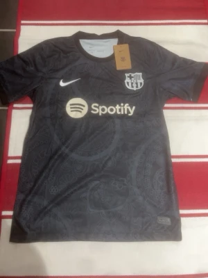 Svart FC Barcelona matchtröja Nike - Snygg svart FC Barcelona matchtröja från Nike med diskret mönster, vita loggor och Spotify som sponsortryck. Tillverkad i lätt och funktionellt Dri-FIT-material som andas, perfekt för träning eller match.