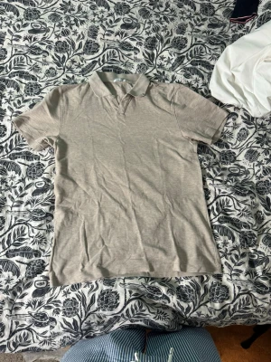Beige pikétröja med krage - Säljer en stilren beige pikétröja med klassisk krage och korta ärmar. Tröjan är enkel och passar till det mesta. Materialet känns mjukt och lätt, perfekt för varmare dagar. Inga synliga loggor eller tryck.
