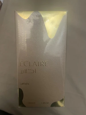 Lattafa Eclaire Eau de Parfum 100ml - Lattafa Eclaire Eau de Parfum i en lyxig, rektangulär förpackning med skimrande guld- och silverdetaljer. Flaskan rymmer 100 ml och har en elegant design som känns exklusiv och modern. Perfekt för dig som gillar stilrena och trendiga parfymer. Den är helt ny och oöppnad. Fortfarande inplastad i sin originalförpackning!