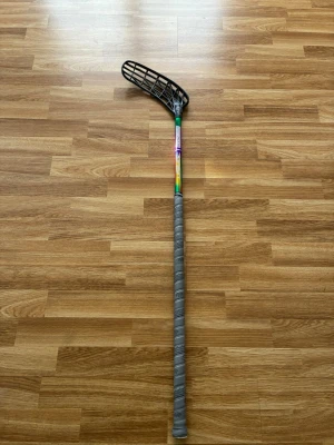Unihoc innebandyklubba EVO LAB - Säljer en Unihoc EVO LAB innebandyklubba med svart blad och färgglad skaftdesign. Klubban har grått grepp och är lätt i materialet, perfekt för snabba spel och bra bollkontroll. Passar dig som vill ha en cool och modern klubba på planen. 149/300 klubban