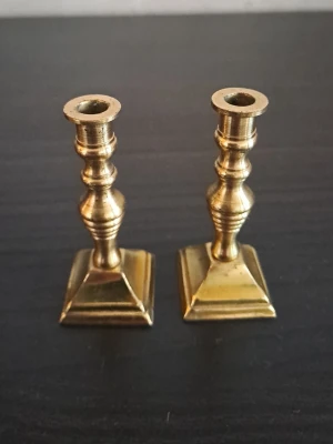 Mini vintage Mässingsljusstakar England, 2-pack - Två klassiska ljusstakar i mässing med fyrkantig fot och dekorativt svarvad form. Märkta med 'ENGLAND' undertill. Perfekta som snygga detaljer i hemmet och passar för vanliga stearinljus. Säljes som par.