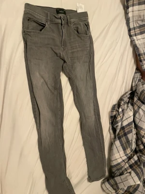 Grå skinny jeans från Replay - Snygga grå skinny jeans från Replay med klassisk femficksdesign och coola detaljer på bakfickorna. Jeansen har en smal passform och är tillverkade i stretchigt denim för extra komfort. Perfekta för en trendig och avslappnad stil.
