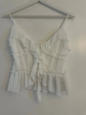 Vit volangig linnetopp med knyt - Superfin vit linnetopp med tunna axelband, volanger och knyt framtill. Justerbara band. Från newyorker. Aldrig använd 